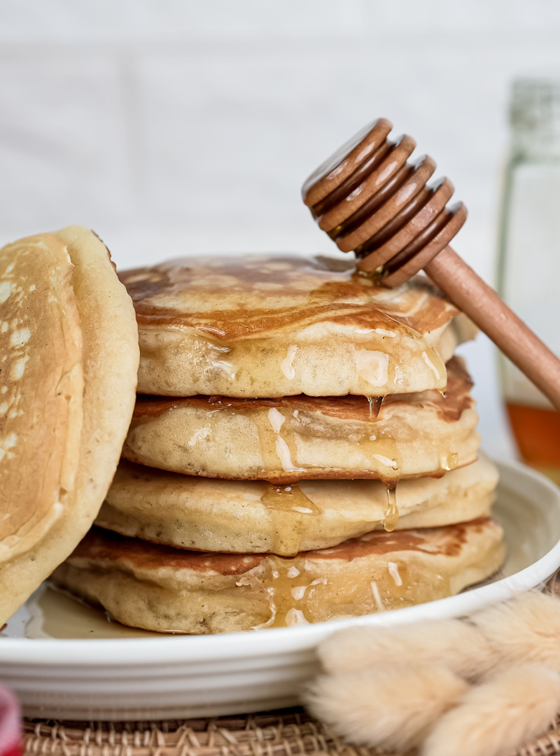 Thick gluten free pancakes covered in honey with wooden honey dipper