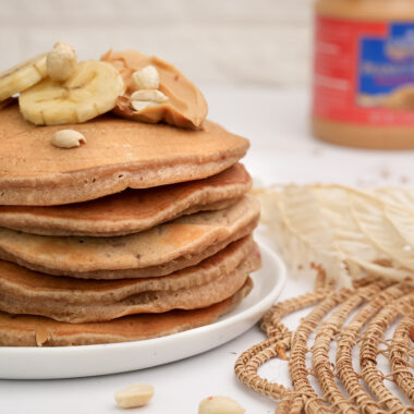 Thick peanut butter pancake stack with banana slices and nuts