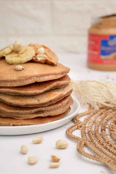 Thick peanut butter pancake stack with banana slices and nuts