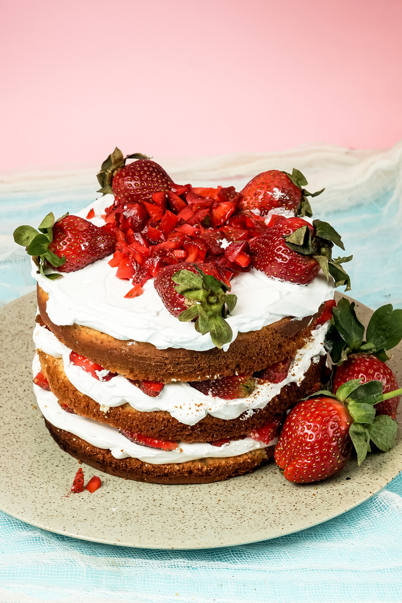 Three-layer strawberry shortcake decorated with fresh strawberries and whipped cream