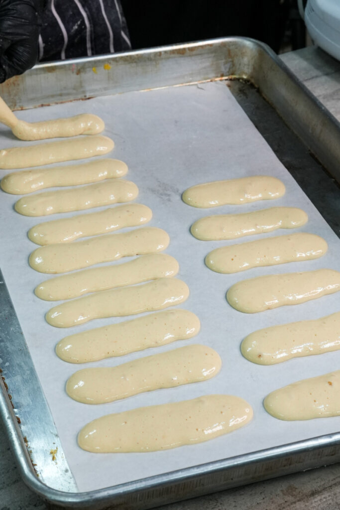 Unbaked ladyfinger cookies arranged on parchment-lined baking tray