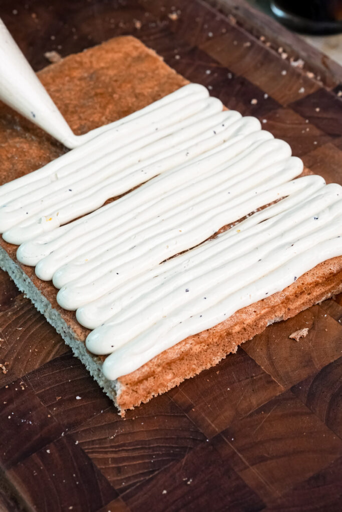 White buttercream being piped in lines on opera cake surface