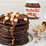 Tall stack of chocolate Nutella pancakes with nuts