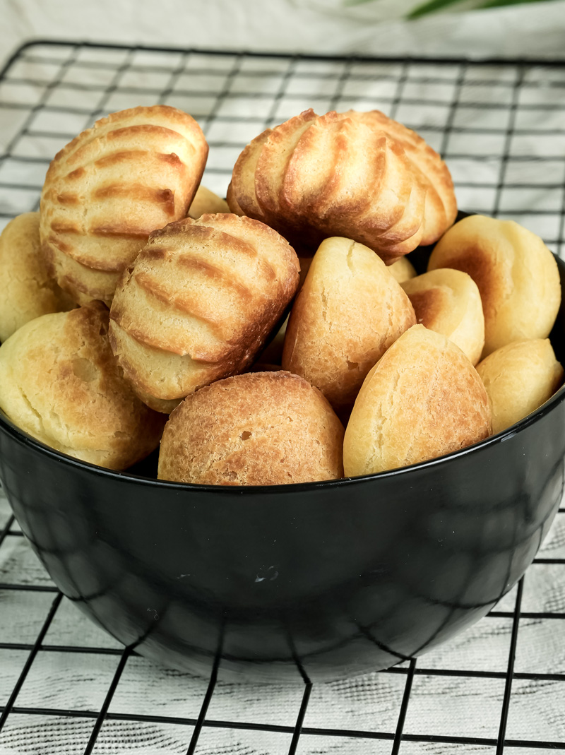 Finished choux pastry puffs in black bowl on cooling rack
