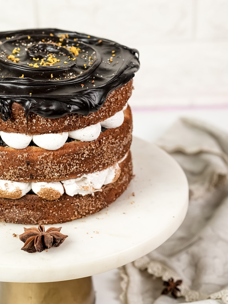 Close-up of churro cake with glossy chocolate ganache dripping down cinnamon sugar sides