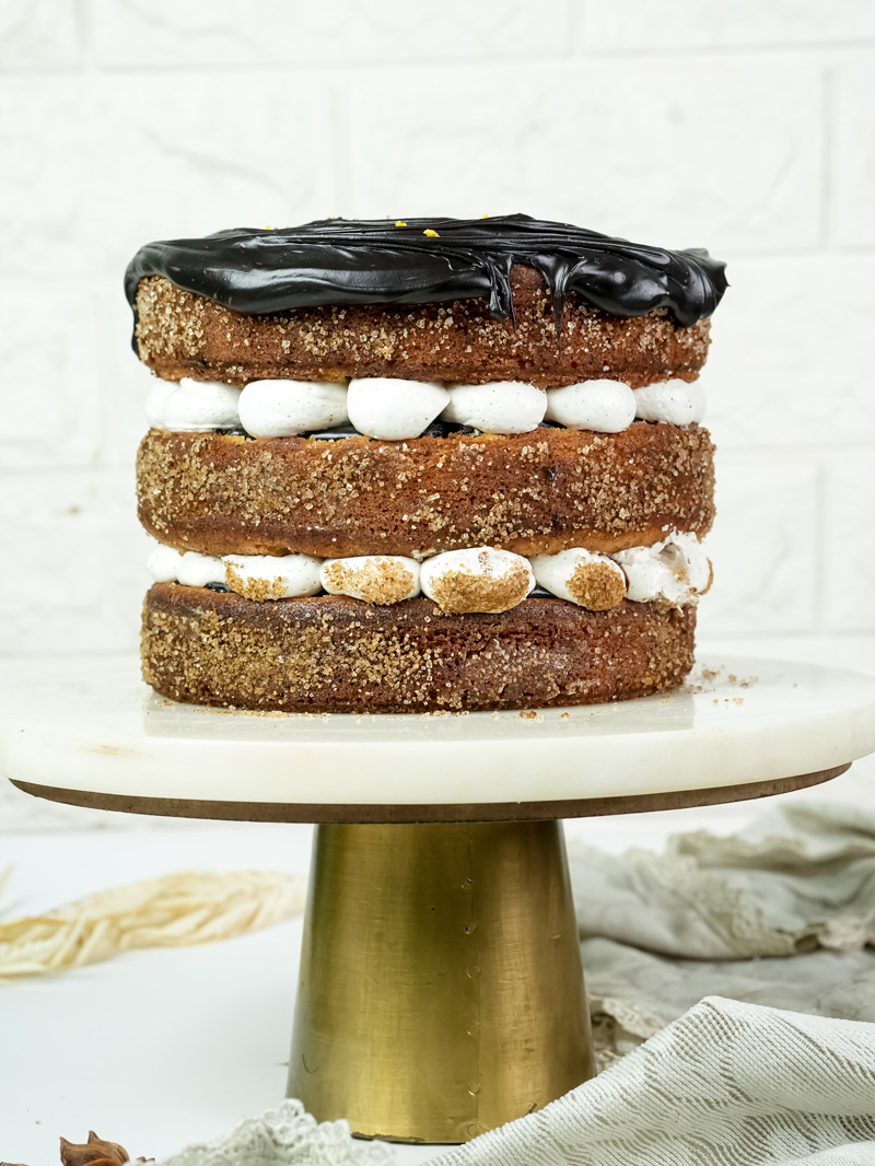 Side view of churro layer cake with piped cream and chocolate ganache topping