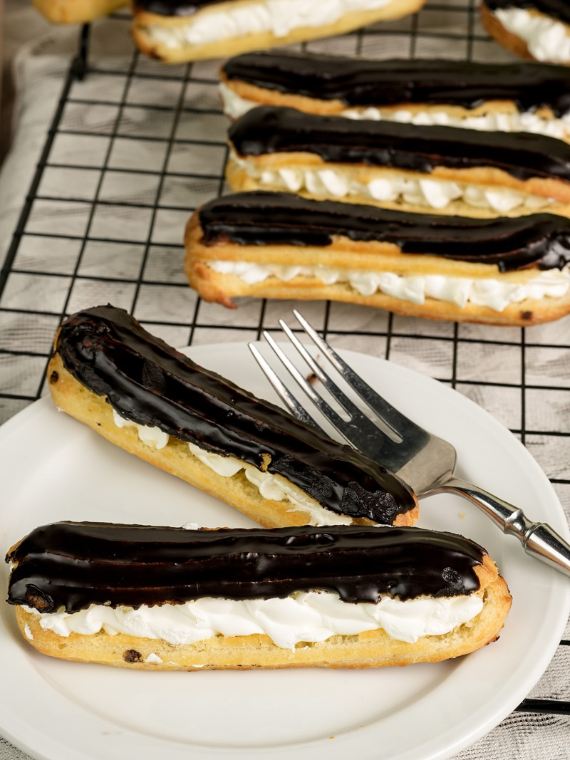 Close-up of cream-filled chocolate eclair served on white plate with fork