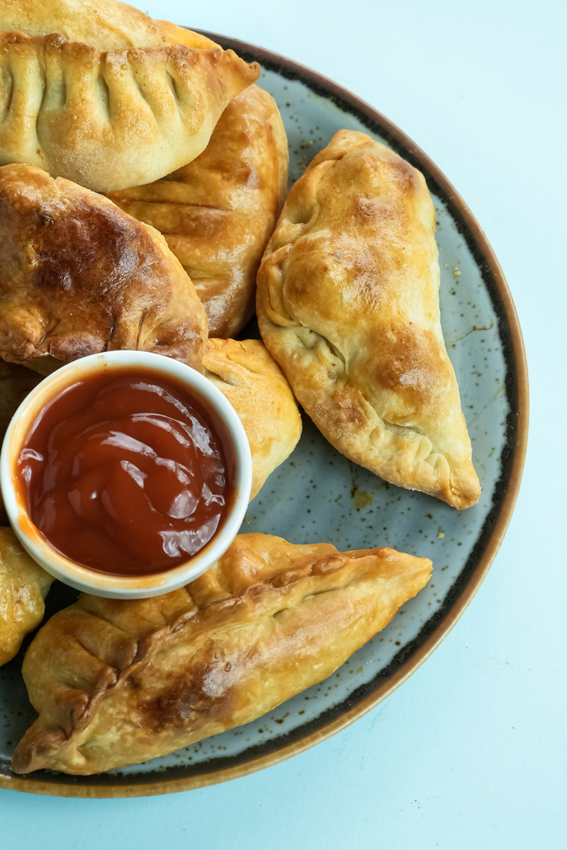 Close-up of golden chicken empanadas with sauce bowl