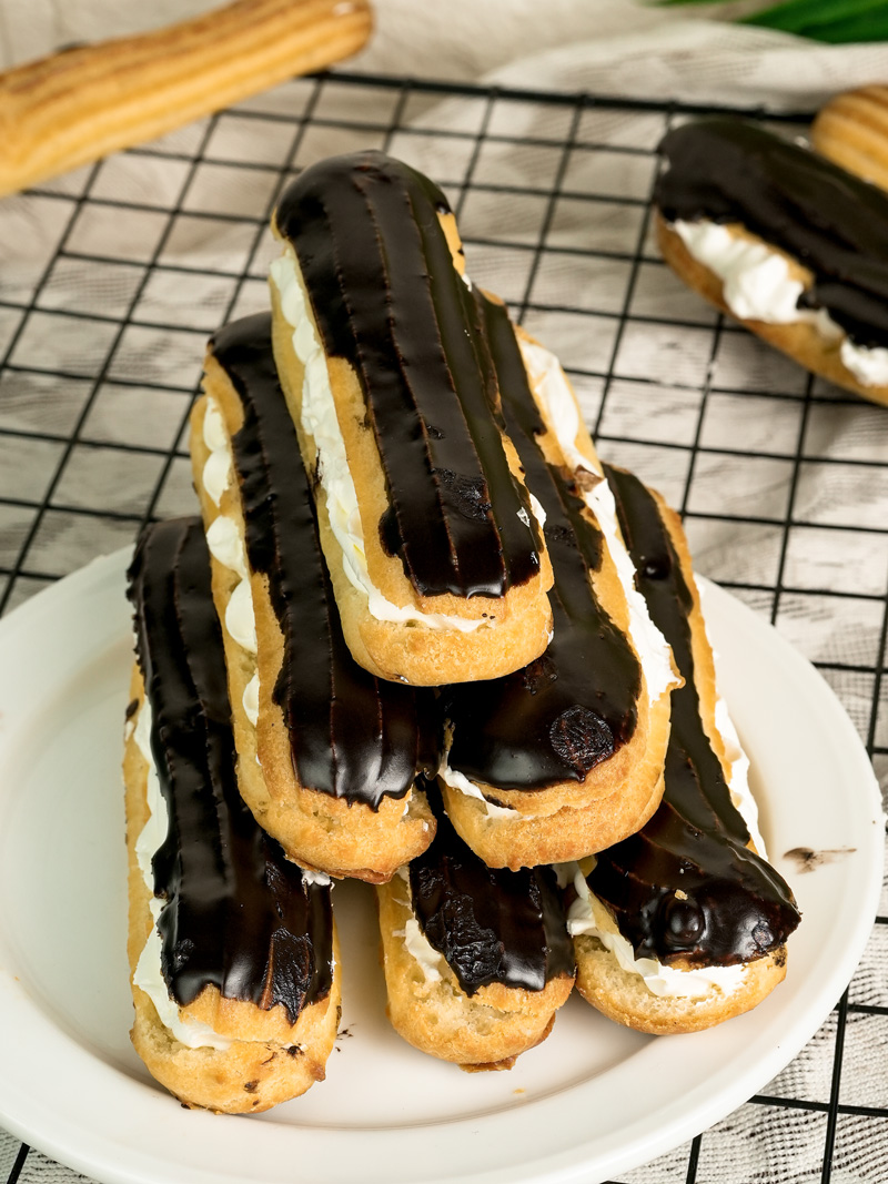 Stack of homemade chocolate eclairs with cream filling on serving plate