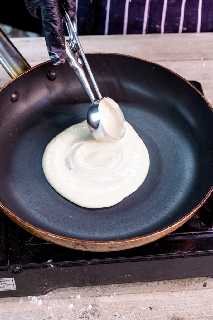 Spreading thin pancake roll batter evenly in cooking pan