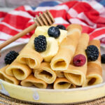 Stack of pancake rolls with berries, butter and wooden honey dipper