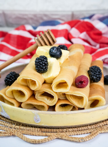 Stack of pancake rolls with berries, butter and wooden honey dipper