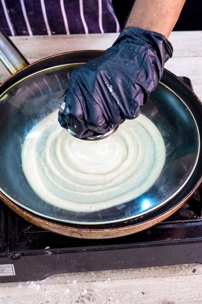 Using ladle to spread pancake roll batter into thin layer