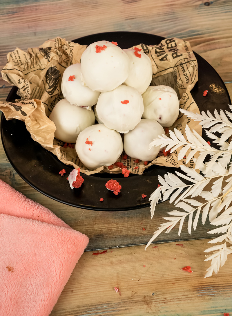 Finished white chocolate coated strawberry cake pops on black serving plate