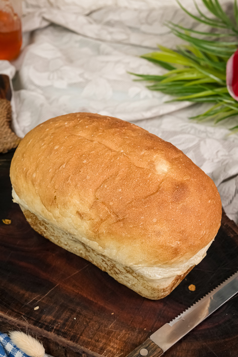 A finished loaf of homemade English Muffin Bread on a wooden board ready to be sliced.