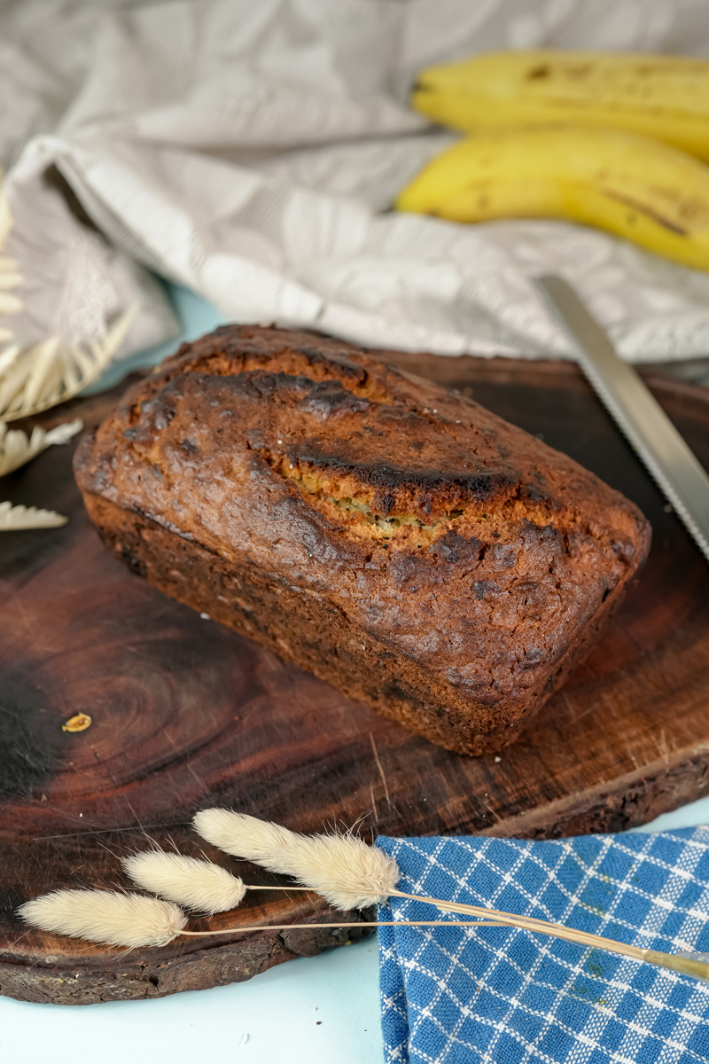 A freshly baked loaf of Hawaiian banana bread on a dark wooden cutting board.