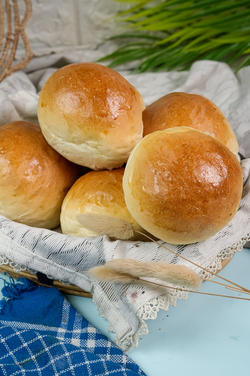 A pile of freshly baked, shiny bread bowls in a cloth-lined basket.