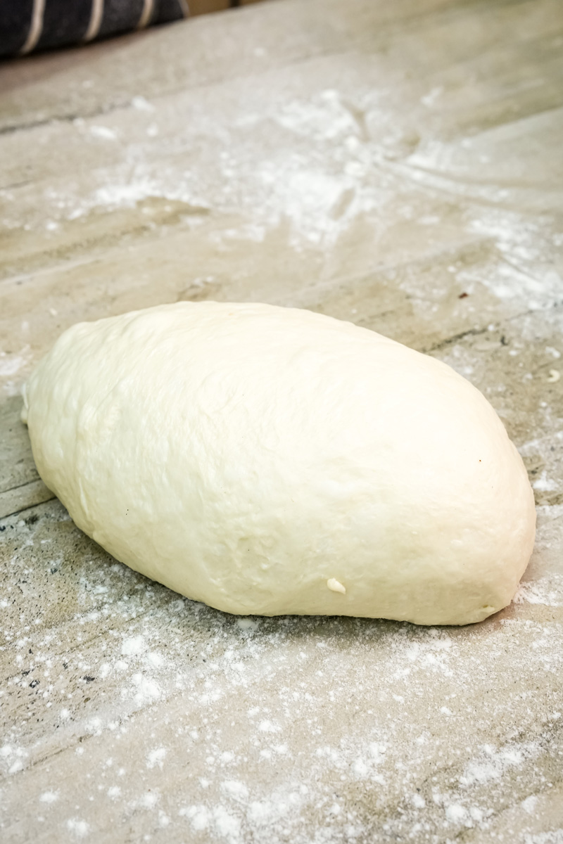 A smooth, shaped loaf of English Muffin Bread dough resting on a floured surface.