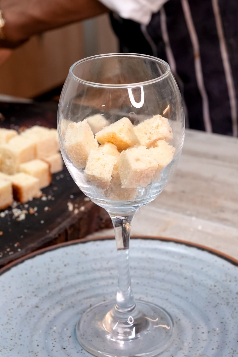Adding cake cubes to wine glass for mango trifle base