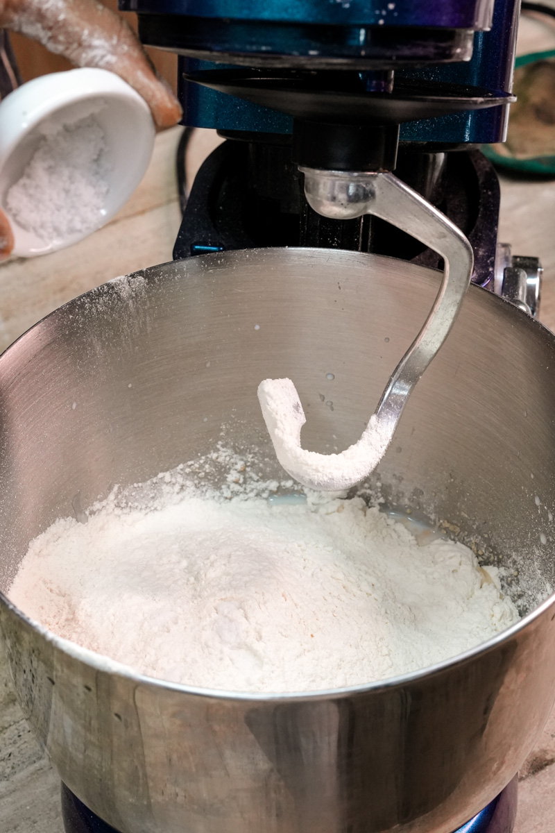 Adding dry ingredients to a stand mixer to make bread bowl dough.