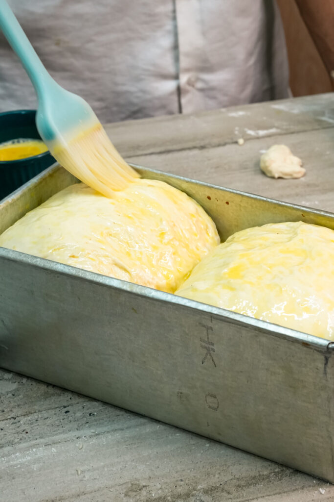 Brushing egg wash on Japanese milk bread before baking