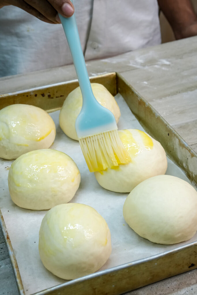 Brushing risen bread bowl dough with egg wash before baking.