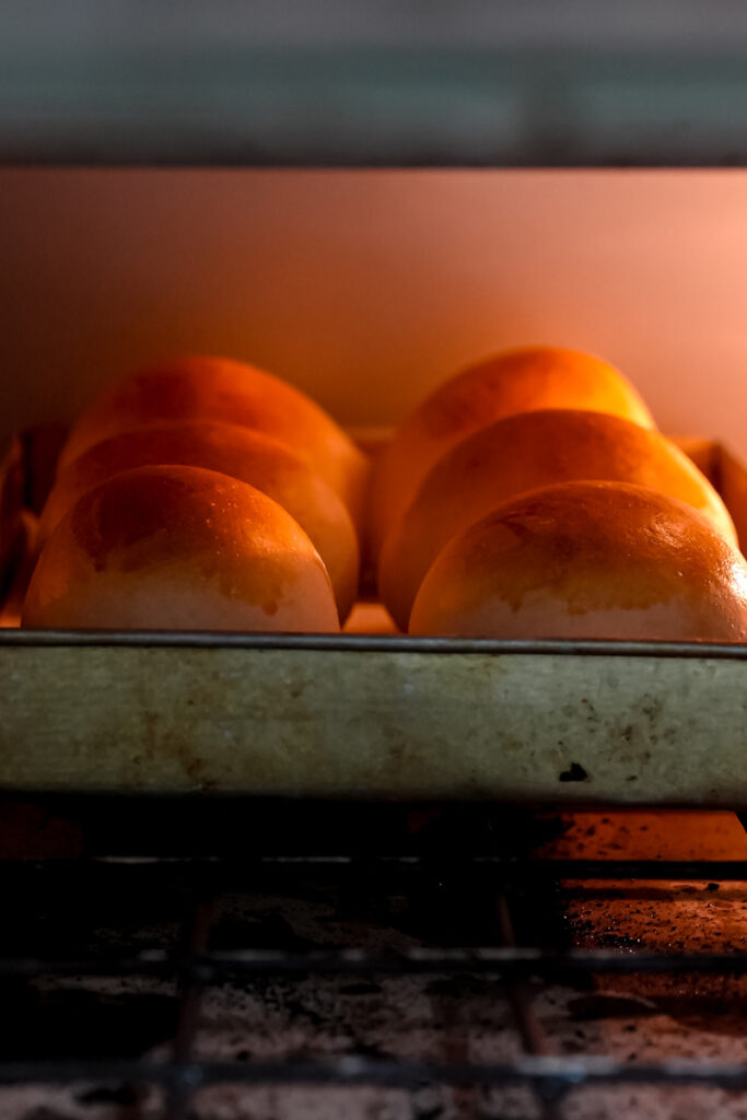 Golden brown bread bowls baking on a tray inside a hot oven.