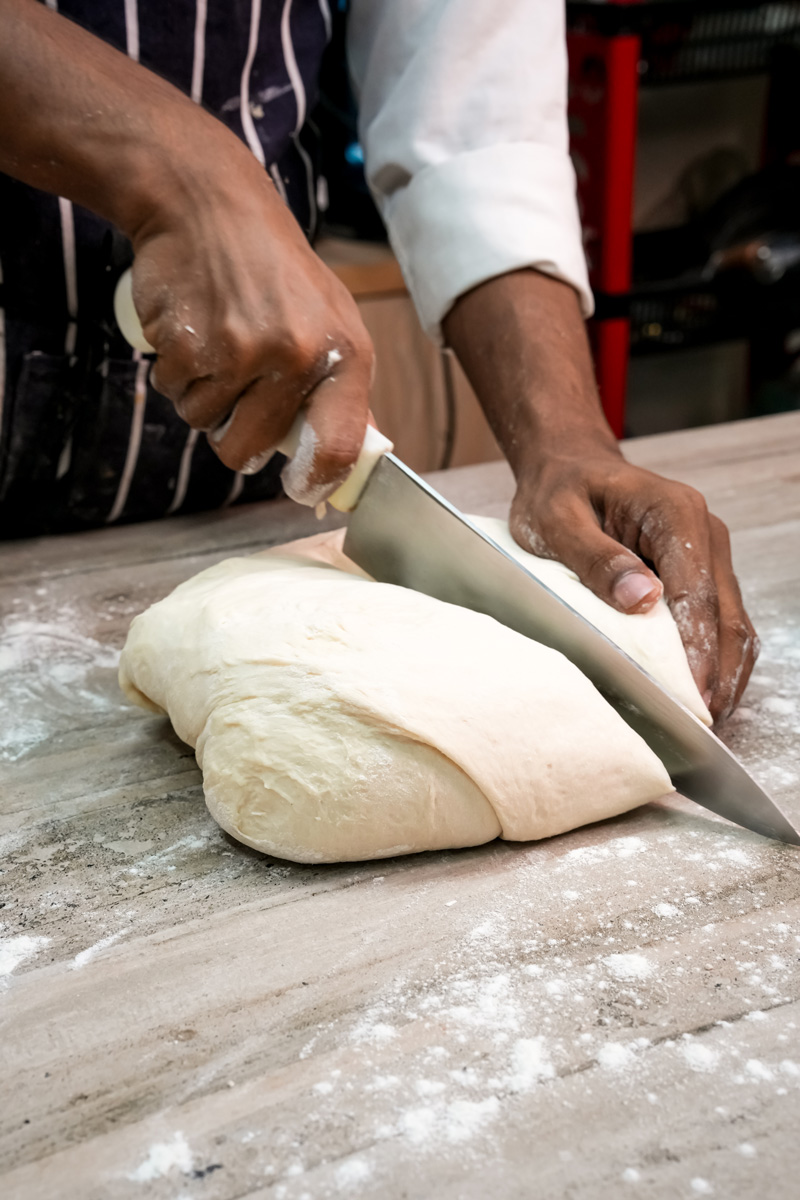 Hands cutting Japanese milk bread dough with bench scraper
