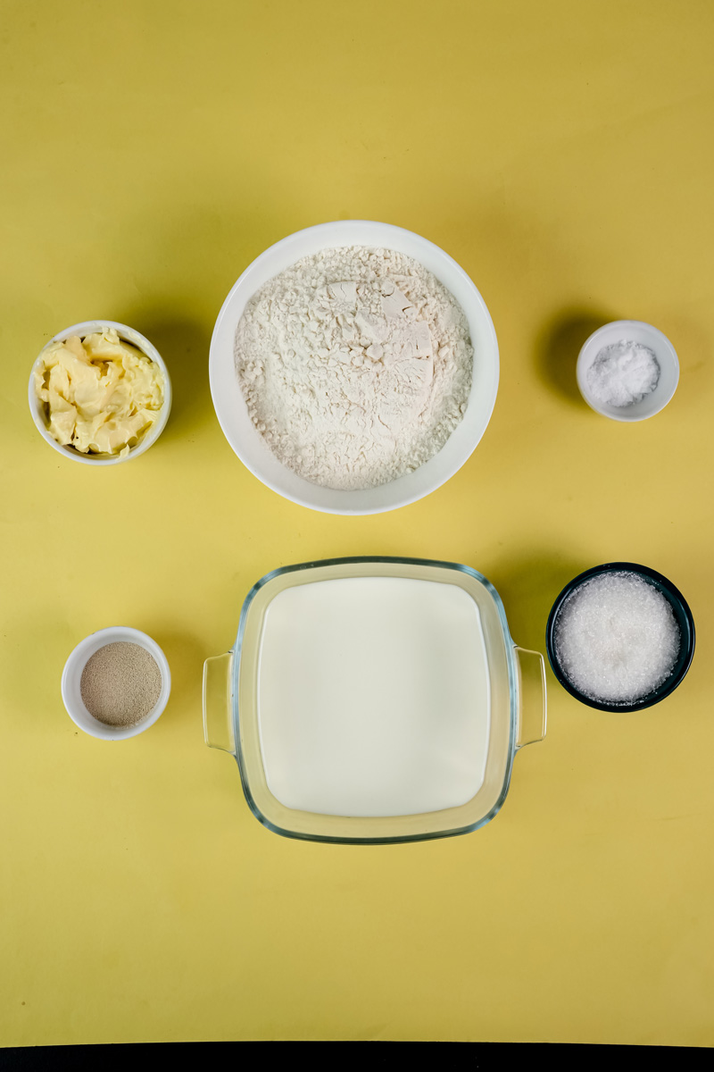 Ingredients for homemade bread bowls laid out, including flour, milk, butter, yeast, and sugar.