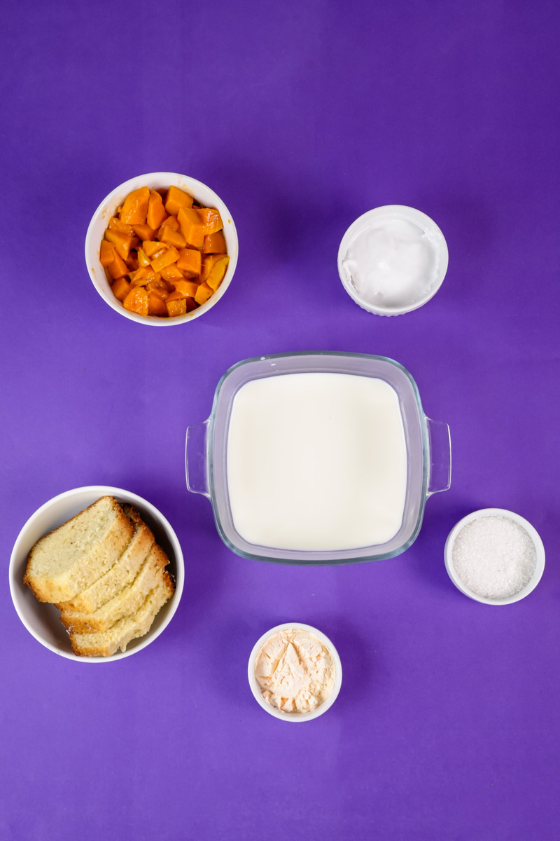 Mango trifle ingredients - diced mango, milk, bread, sugar and flour on purple background