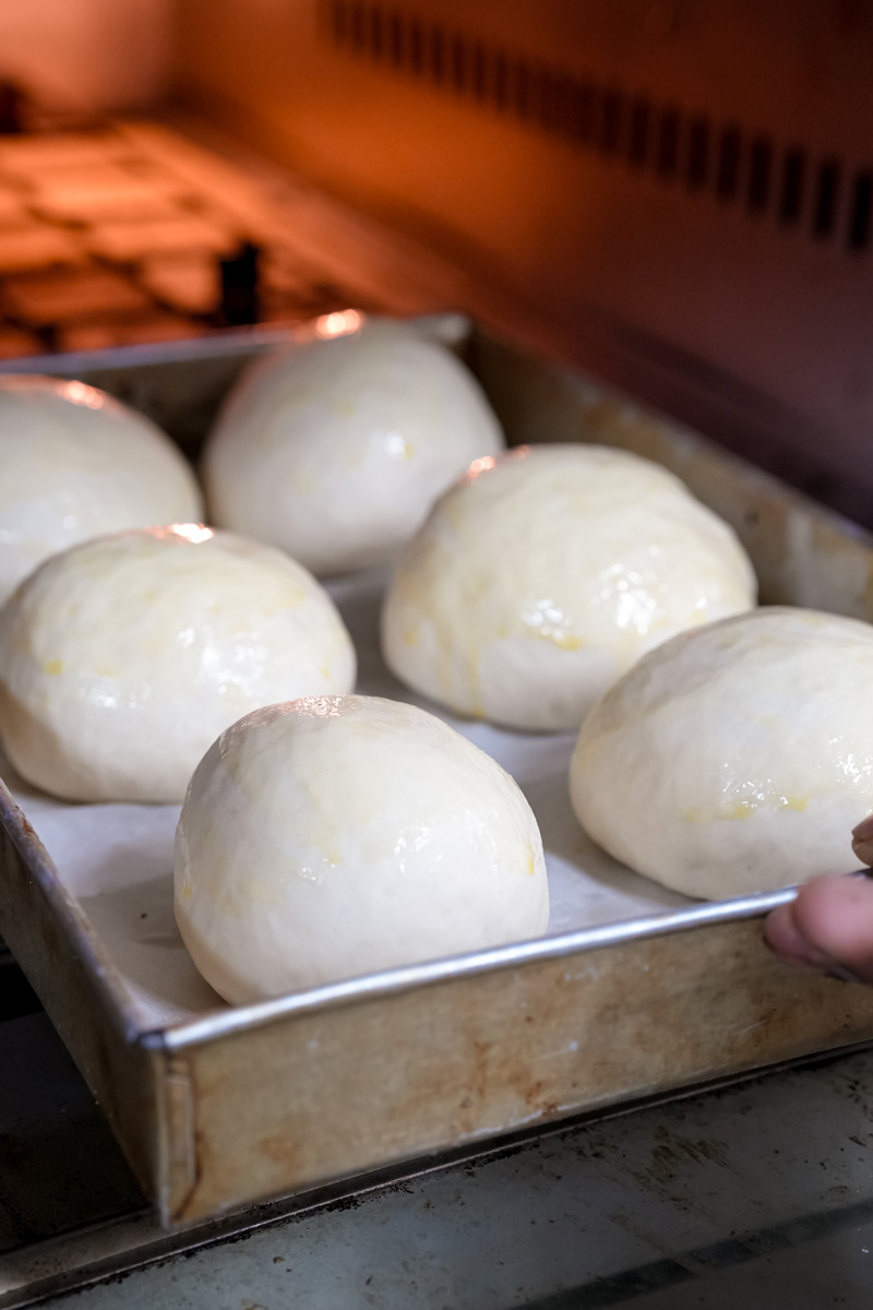 Placing the tray of bread bowl dough into a hot oven.