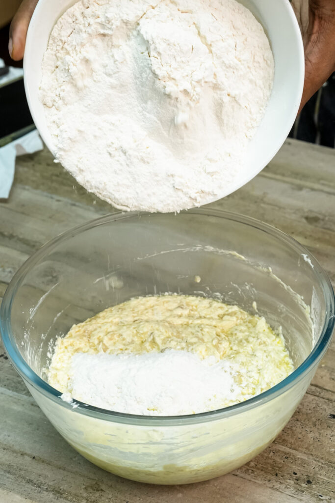 Pouring flour into the wet ingredients to make the Hawaiian banana bread batter.