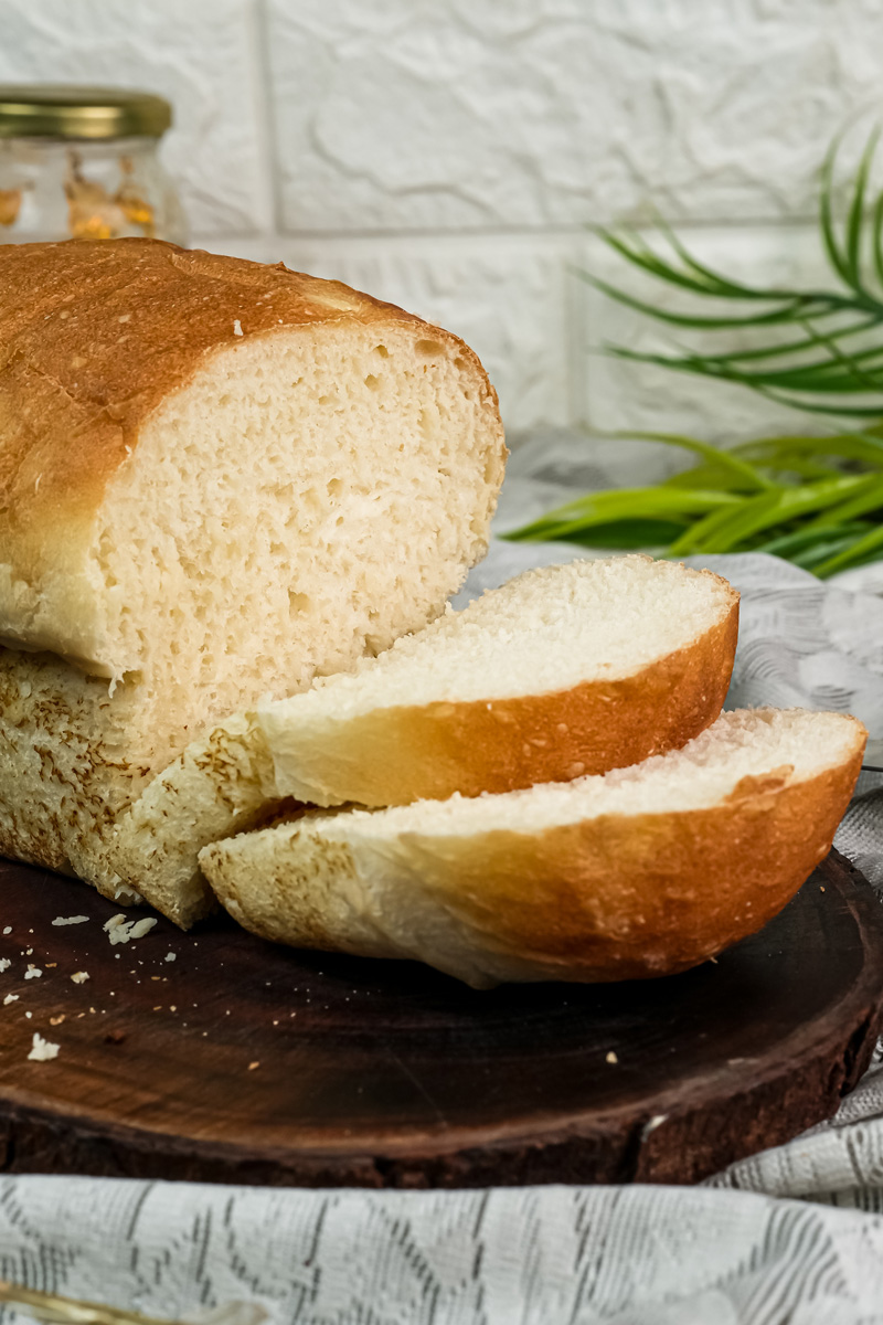 Two thick slices of homemade English Muffin Bread next to the partially sliced loaf.