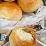 A spoon taking a scoop of creamy soup from a hollowed-out bread bowl.