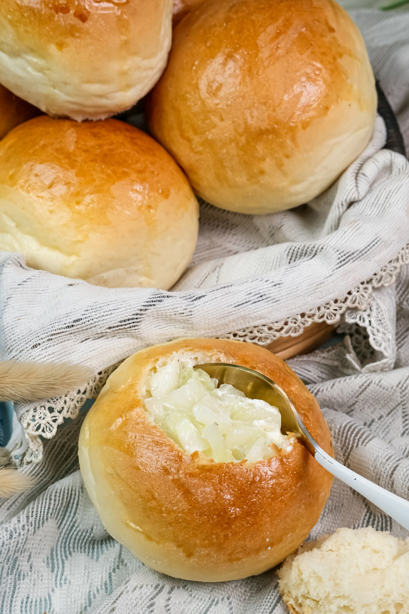 A spoon taking a scoop of creamy soup from a hollowed-out bread bowl.