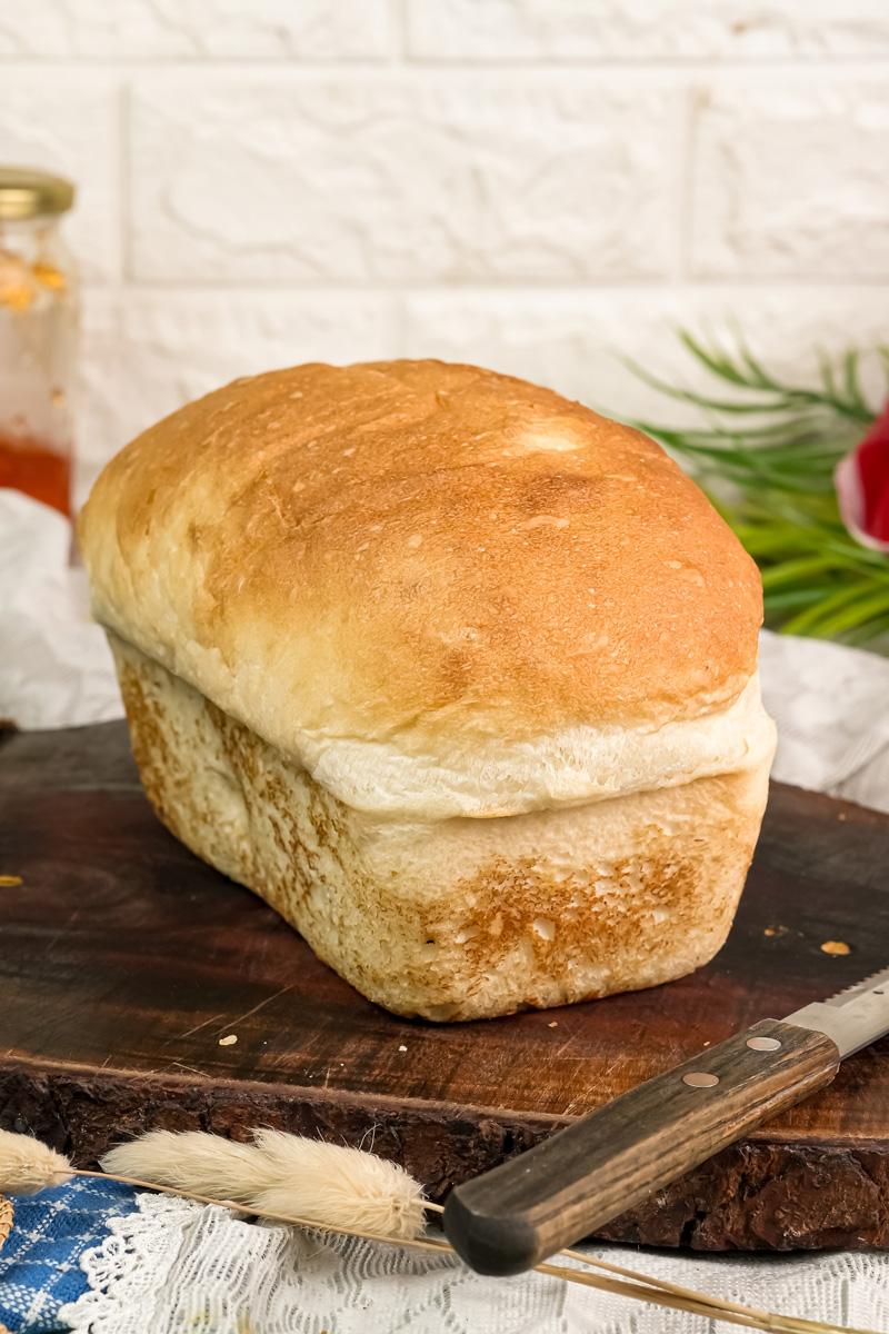 A whole, baked loaf of English Muffin Bread on a wooden cutting board.