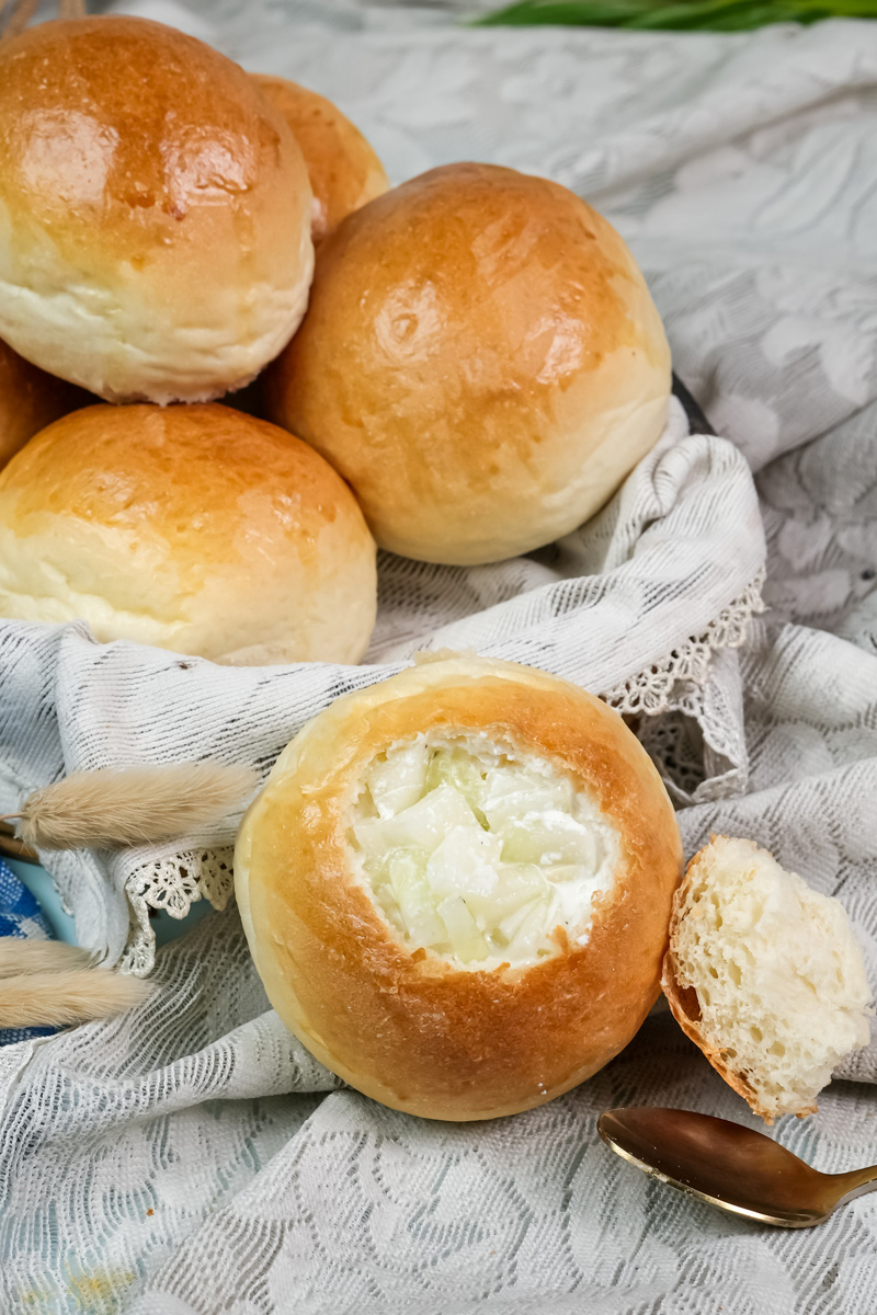A homemade bread bowl filled with creamy onion soup, with the top resting beside it.