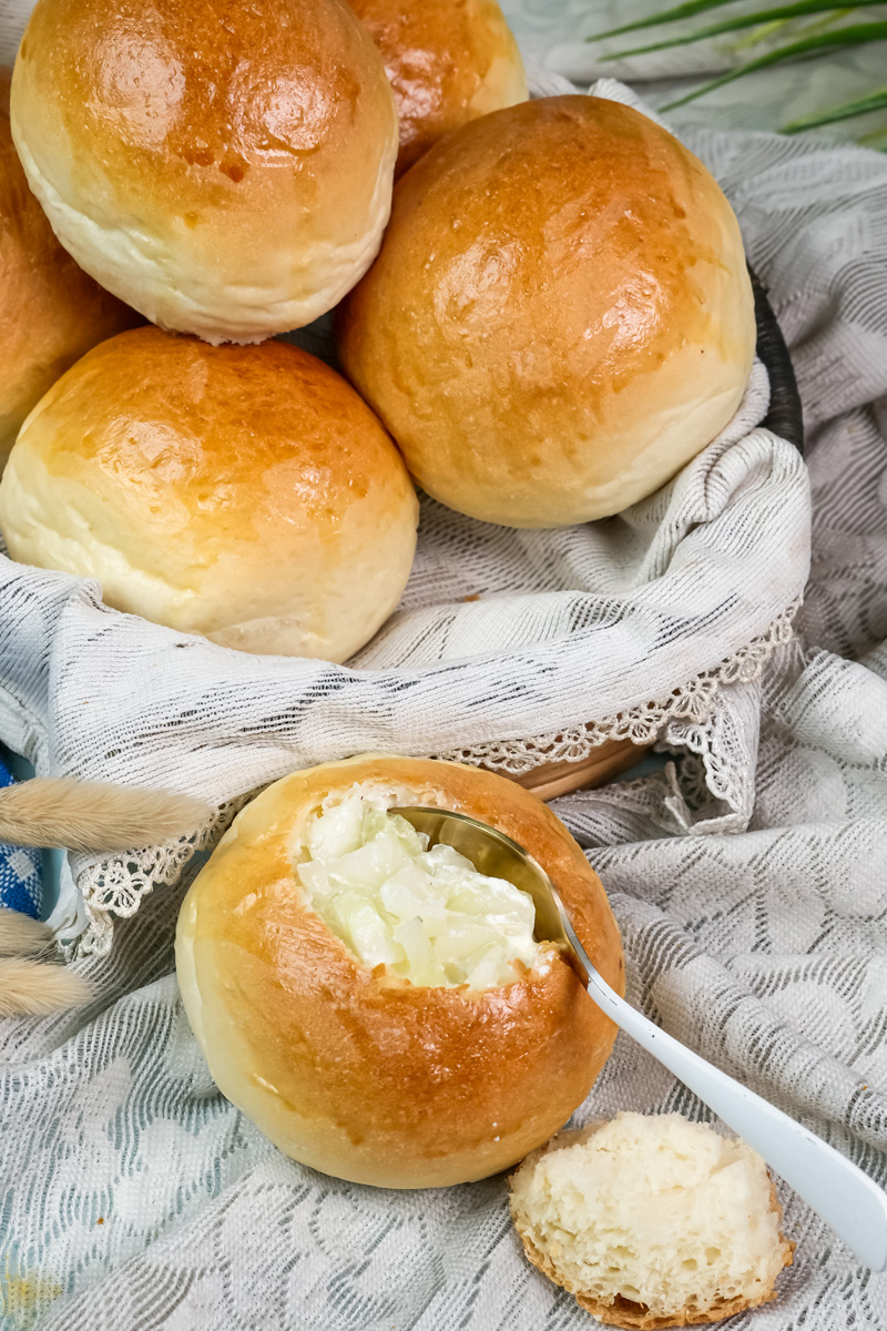 A homemade bread bowl filled with soup, ready to eat with a spoon.