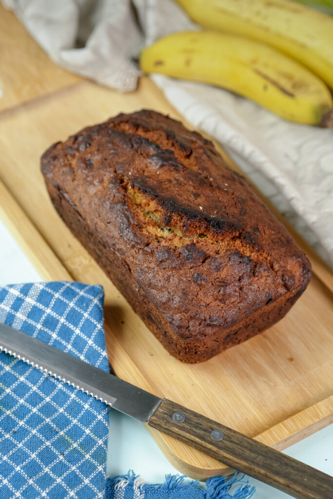 A perfect loaf of homemade Hawaiian banana bread on a bamboo board with a knife.