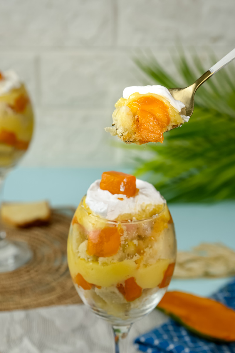 Taking spoonful of layered mango trifle dessert