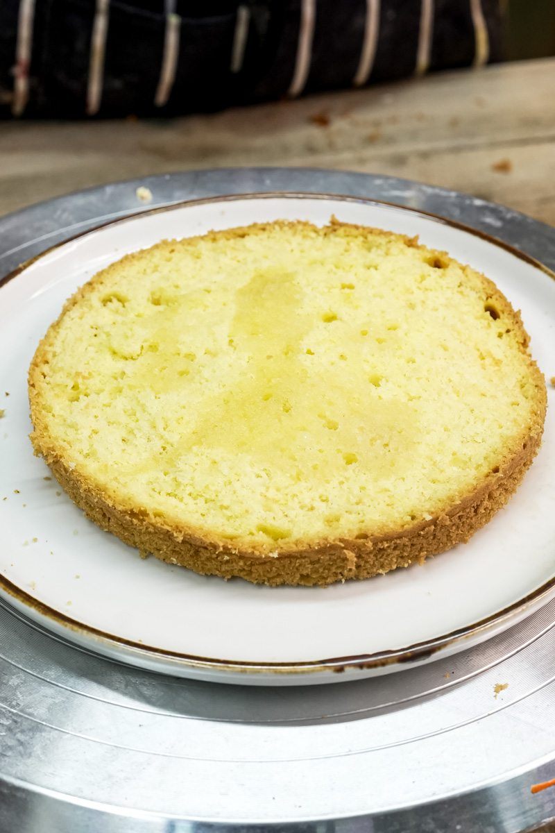 A baked sponge cake layer on a white plate, ready for frosting