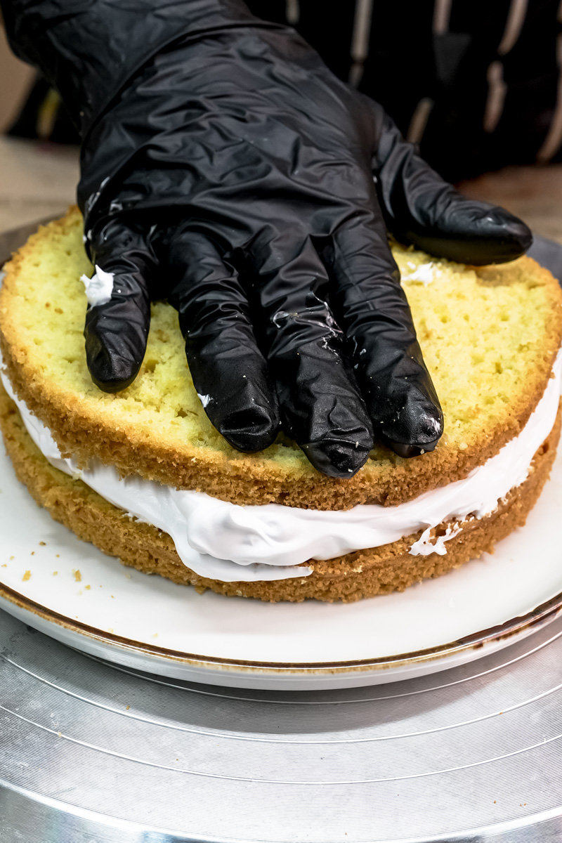 A baker adding a second layer of cake to a frosted first layer to create a drip cake