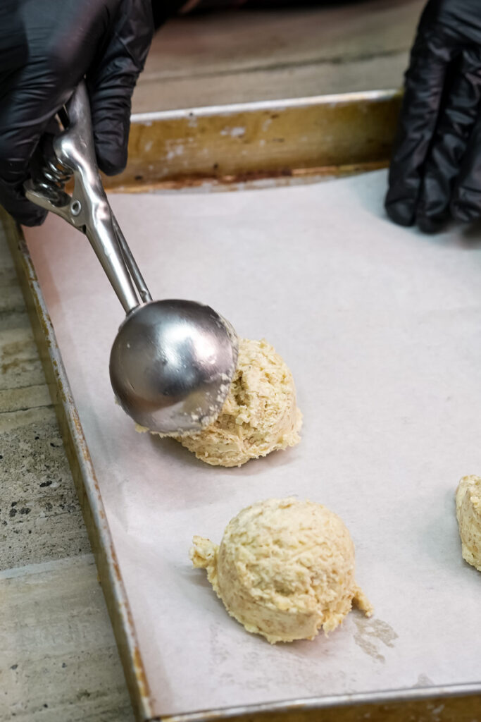 A cookie scoop placing a ball of oatmeal cookie dough onto a parchment-lined baking sheet