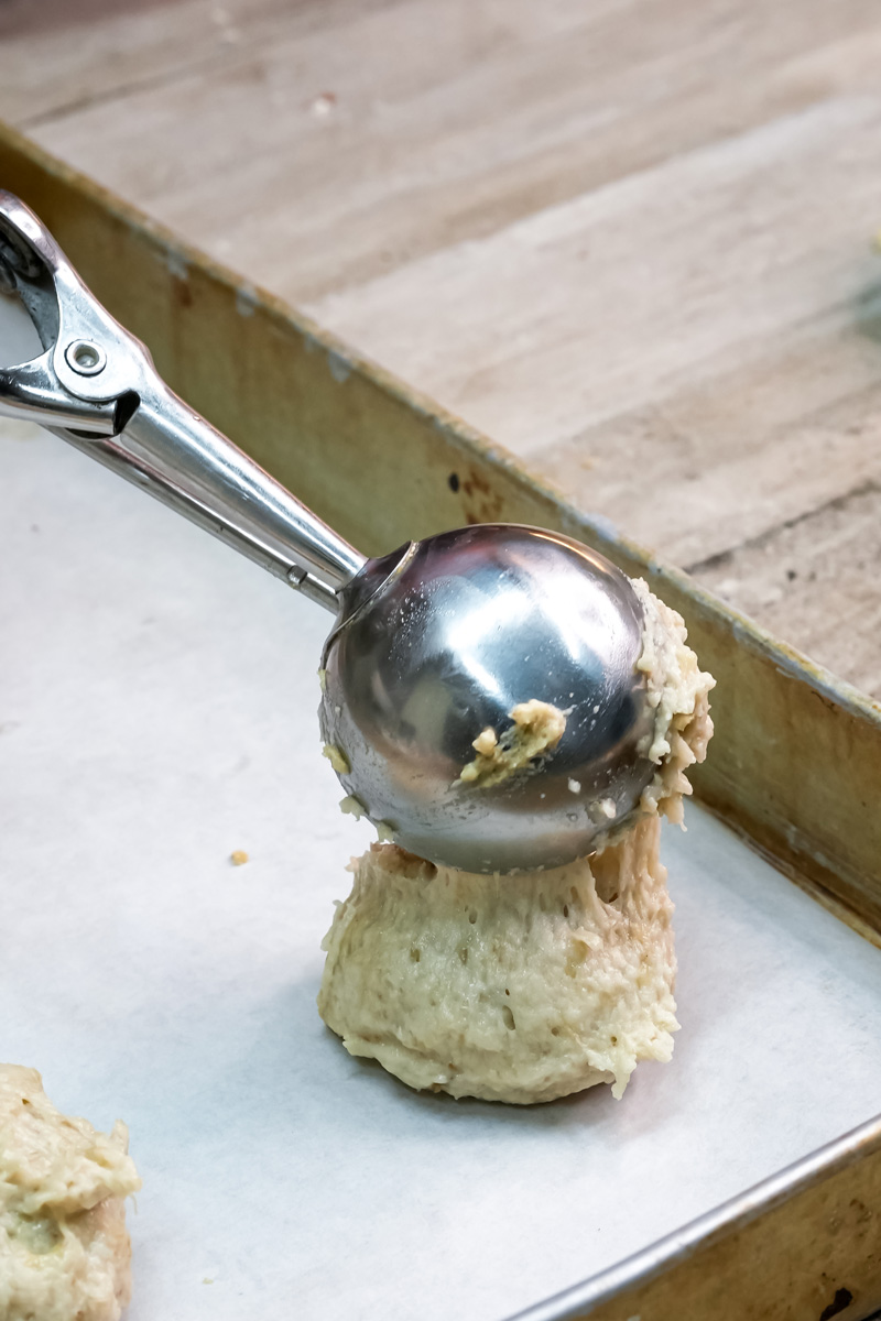 A cookie scoop releasing a portion of banana cookie dough onto a parchment-lined baking sheet