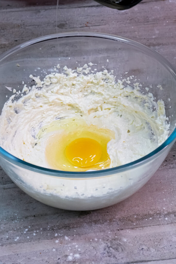 A cracked egg yolk is added to the creamed butter and sugar mixture in a glass bowl