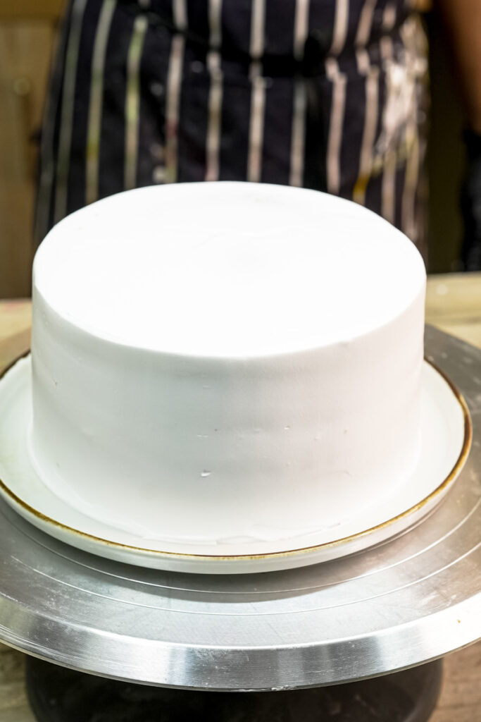 A finished drip cake fully frosted with smooth white buttercream