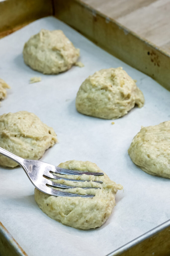 A fork gently pressing down on a scoop of banana cookie dough on a baking sheet