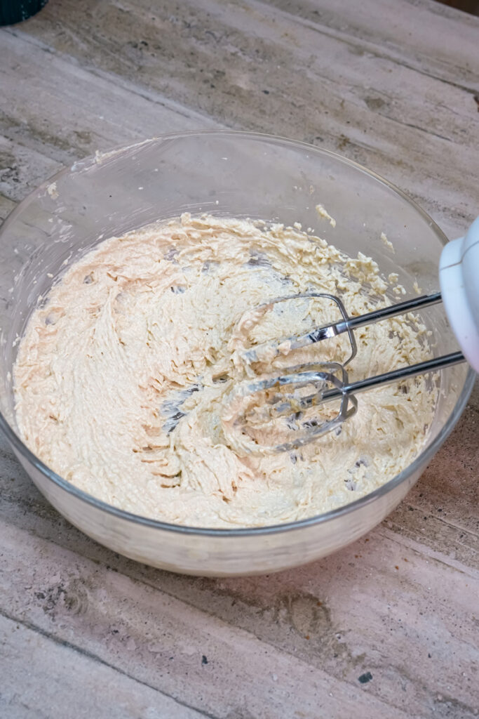 A hand mixer creaming butter and sugars together in a glass bowl