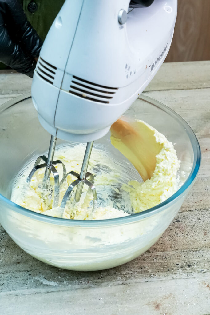 A hand mixer creaming softened butter in a glass bowl to prepare the cookie dough