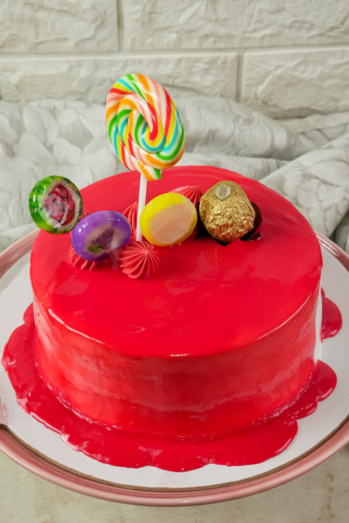 A red drip cake with a colorful lollipop and chocolates on top